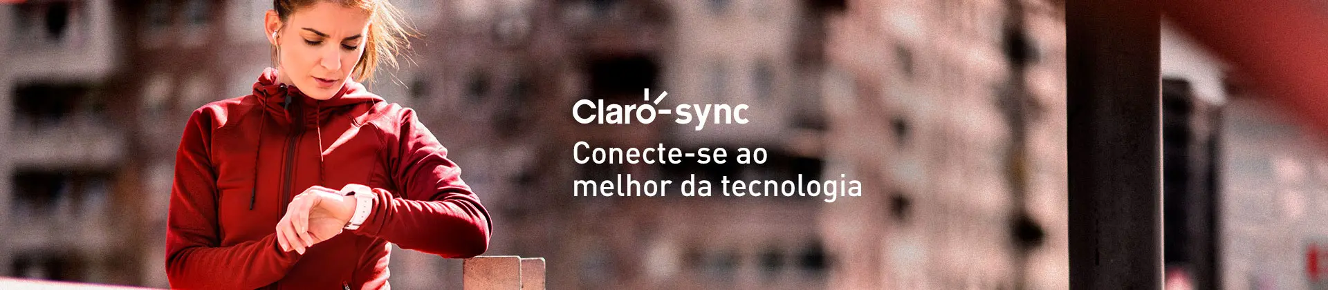 Mulher vestindo casaco vermelho em estilo esportivo e calça preta, usando fones de ouvindo e checando o seu smartwatch que está no pulso. Ela está em um ambiente externo.