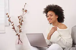 Imagem de uma moça sorrindo com as mãos no peito em frente a um notebook.