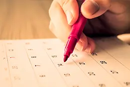 Imagem de uma mão com um caneta vermelha sob um calendário;