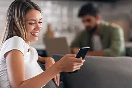 Imagem de uma moça sorrindo e olhando para um celular.