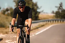 Foto de um rapaz andando de bicicleta. Ele usa capacete e óculos escuros.
