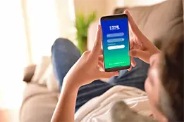 Imagem de um rapaz desfocado deitado no sofá com um celular na mão.