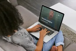 Uma moça sentada no sofá e um notebook no colo.