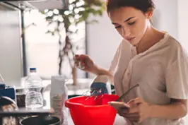 Imagem de uma moça cozinhando enquanto faz consultas no celular.