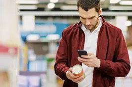 Um rapaz jovem mirando um celular em um produto de supermercado.