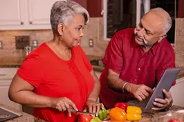 Um casal cozinhando na cozinha com o auxílio de um tablet.