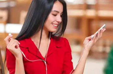 Imagem de uma moça com fones de ouvido e um celular nas mãos.