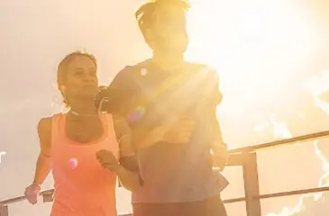 Um casal jovem fazendo corrida junto e os raios do sol estão em destaque na imagem.