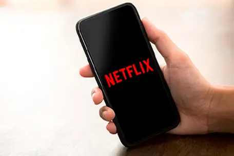 Mão segurando celular com logo Netflix.