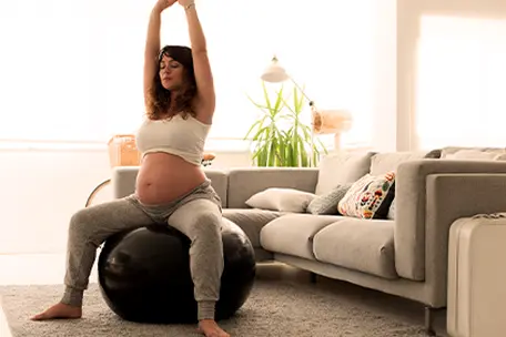 Uma moça grávida se exercitando sentada em uma bola.