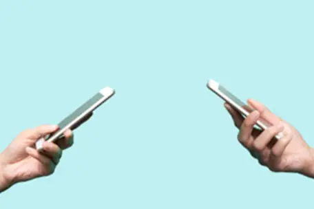Duas mãos, uma de frente para outra. Ambas segurando um celular com um fundo azul.