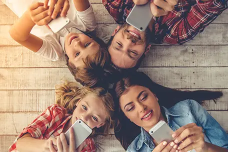 Imagem de uma família, marido, esposa e filhos deitados mexendo em aparelhos celulares.