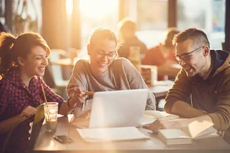 Três jovens sorrindo enquanto olham para um notebook.
