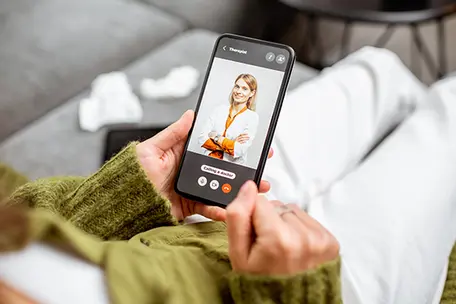 Imagem de uma pessoa desfocada com o celular em mãos em ligação com uma profissional da saúde.
