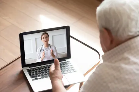 Imagem de um senhor consultando um profissional da saúde pela tela de um notebook.