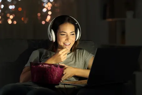 Imagem de mulher comendo pipoca e olhando para a tela do notebook.