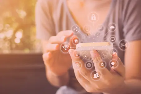 mão feminina segurando um celular e em volta do aparelho vários ícones que representam conexão e tecnologia